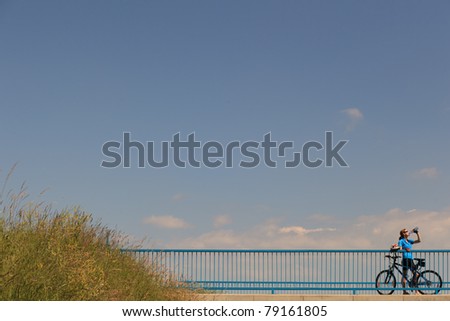 Background for poster or advertisment pertaining to cycling/sport/outdoor activities - female cyclist during a halt on a bridge against blue sky (color toned image)