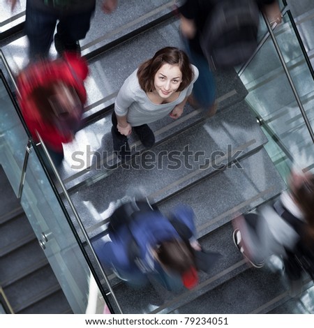 At the university/college - Students rushing up and down a busy stairway - confident pretty young female student looking upwards (color toned image)