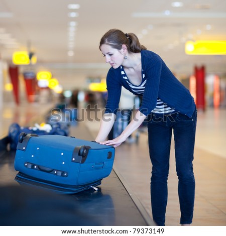 Baggage reclaim at the airport - pretty young woman taking her suitcase off the baggage carousel (color toned image)