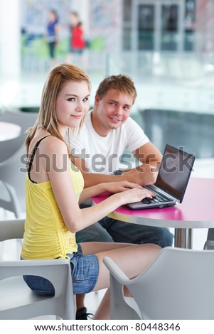 two college students having fun studying together, using a computer in a university library/study room (shallow DOF, color toned image)