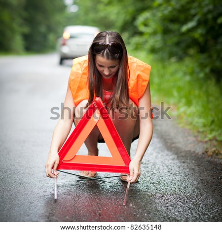 Young female driver wearing a high visibility vest/safety vest, putting in place the warning triangle after her car has broken down