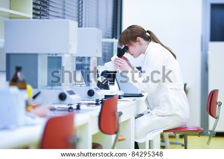 pretty female researcher using a microscope in a lab