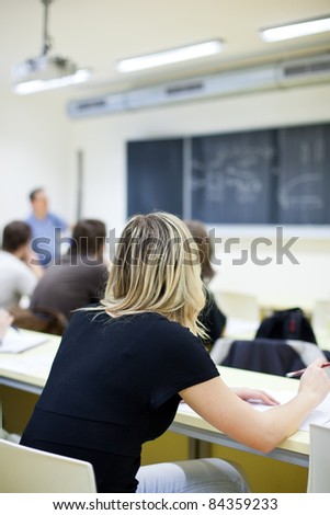 young pretty female college student sitting in a classroom full of students during class (shallow DOF; color toned image)