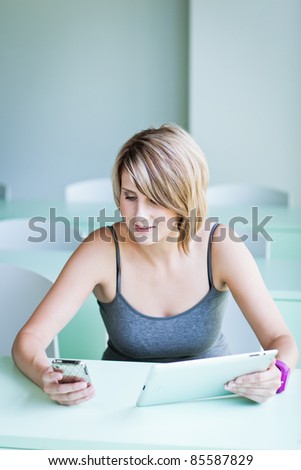 Pretty college student/businesswoman using her cell phone and a tablet computer (shallow DOF; color toned image)