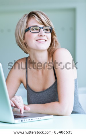 Portrait of a young woman pensively looking out of the window while sitting in front of her laptop
