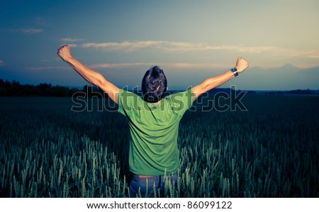 Young man enjoying his freedom/rejoicing from his success in the countryside, in a wheat field at dusk (color toned image)