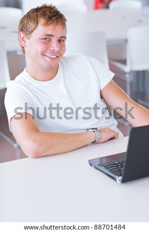 Happy handsome young male college student  using his computer in the campus common area/high school study room (shallow DOF, color toned image)