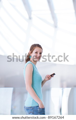 Pretty, young woman/college student using her mobile phone/speaking on the phone in a public area (shallow DOF; color toned image)