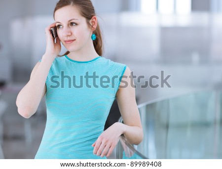Pretty, young woman using her mobile phone/speaking on the phone in a public area (shallow DOF; color toned image)