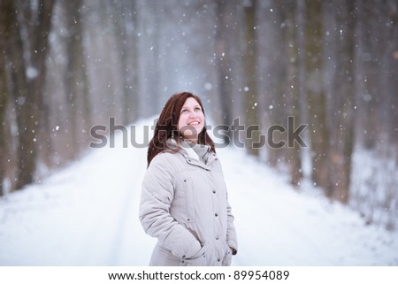 Enjoying the first snow: young woman outdoors on a lovely forest path watching the snowflakes falling (color toned image)