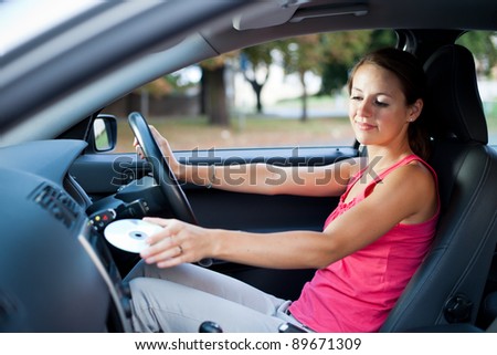 Young female driver playing music in the car - changing CDs (color toned image; shallow DOF)