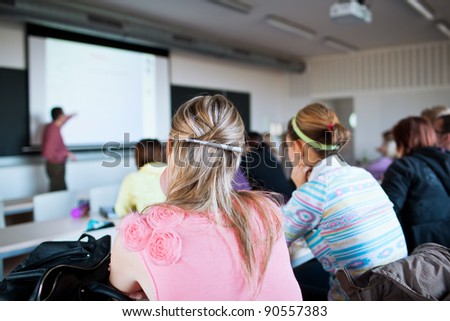young, pretty female college student sitting in a classroom full of students during class (shallow DOF; color toned image)