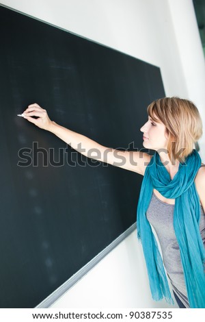 pretty young college student/young teacher writing on the chalkboard/blackboard during a math class (color toned image; shallow DOF)