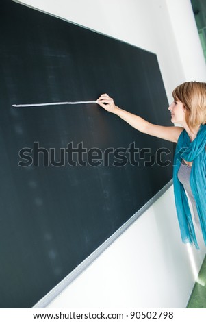 Pretty young college student/teacher writing on the chalkboard/blackboard during a math class (color toned image; shallow DOF)