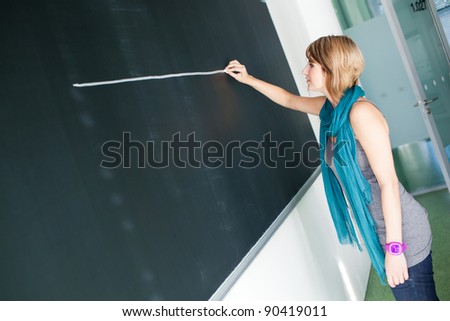 pretty young college student/young teacher writing on the chalkboard/blackboard during a math class (color toned image; shallow DOF)