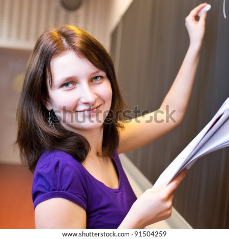 pretty young college student writing on the chalkboard/blackboard during a math class