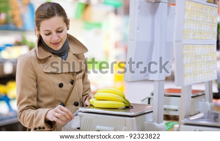 Beautiful young woman shopping for fruits and vegetables in produce department of a grocery store/supermarket - buying bananas (shallow DOF; color toned image)