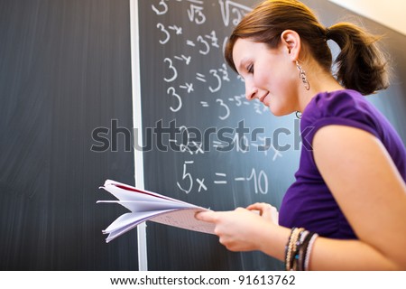 pretty young college student/young teacher writing on the chalkboard/blackboard during a math class