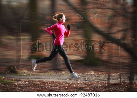 Young woman running outdoors in a city park on a cold fall/winter day (motion blurred image; color toned image)