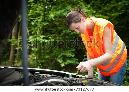 Young female driver wearing a high visibility vest, bending over the engine of her broken down car