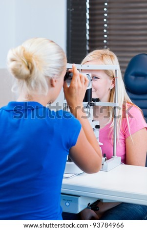 optometry concept - pretty, young female patient having her eyes examined by an eye doctor (color toned image; shallow DOF)