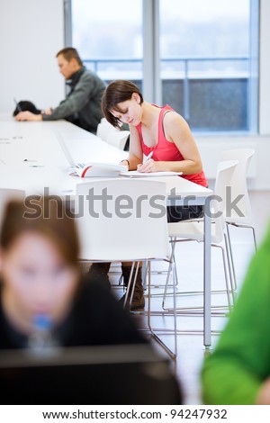 Pretty young college student studying in the library/a study room at campus (shallow DOF)