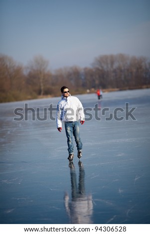 Handsome young man ice skating outdoors on a pond (color toned image; shallow DOF)
