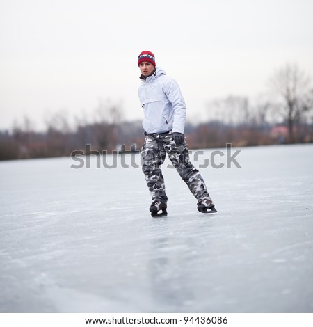 Handsome young man ice skating outdoors on a pond on a cloudy winter day (color toned image; shallow DOF)