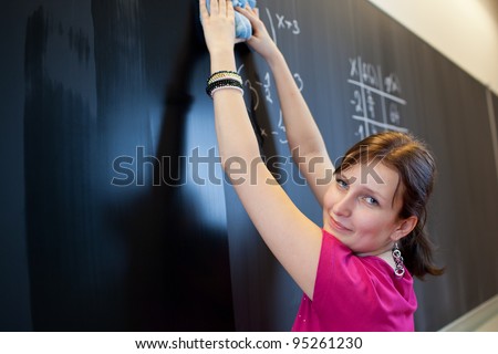 pretty young college student erasing the chalkboard/blackboard during a math class (color toned image; shallow DOF)