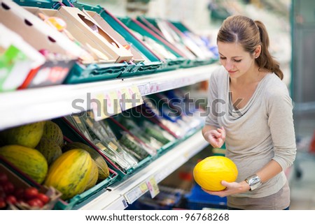 Beautiful youn woman shopping for fruits and vegetables in produce department of a grocery store/supermarket (shallow DOF; color toned image)