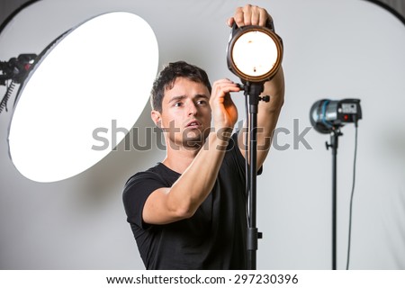 Young, pro photographer setting lights in his well equipped studio before a photo shoot (color toned image; shallow DOF)