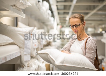 Pretty, young woman choosing the right pillow for her bed in a modern home furnishings store (color toned image; shallow DOF)