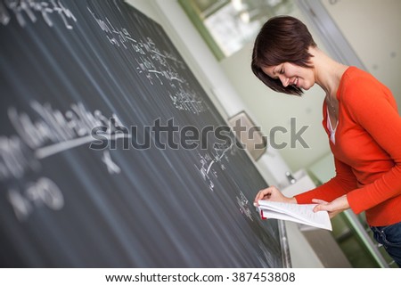 Pretty young college student/young teacher writing on the chalkboard/blackboard during a math class (color toned image)