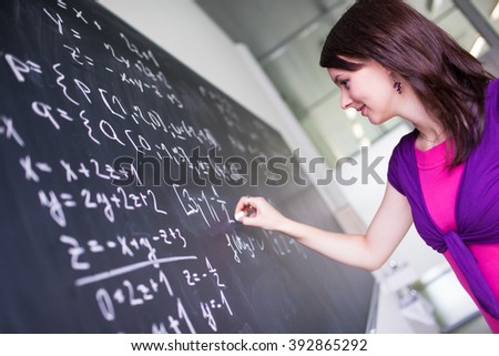 Pretty, young college student writing on the chalkboard/blackboard during a math class
