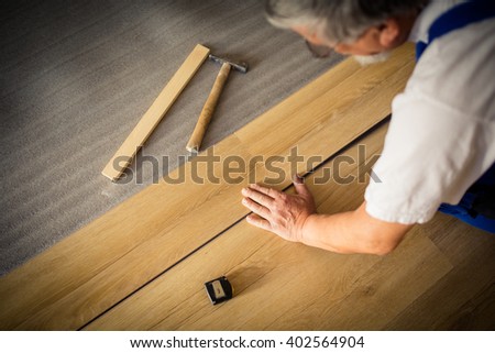 DIY, repair, building and home concept - close up of male hands lying parquet floor board/laminate flooring (shallow DOF; color toned image)