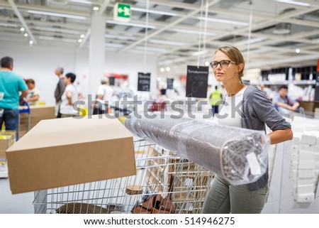Pretty, young woman choosing the right furniture for her apartment in a modern home furnishings store - with a trolley, done shopping, leaving the store, going home with the purchased goods