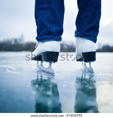Young woman ice skating outdoors on a pond on a freezing winter day - detail of the legs (color toned image)