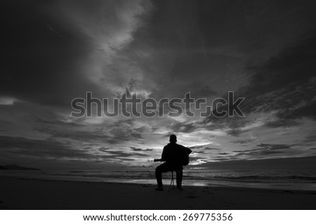 Silhouette Guitar player on the beach at sunset (Black and White) Image has grain or blurry or noise and soft focus when view at full resolution.  (Shallow DOF, slight motion blur)