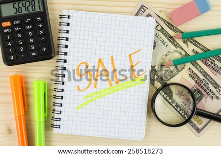 Notebook with sale word and office tools on wooden table
