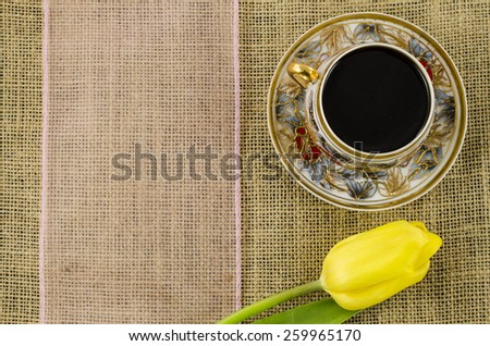 Porcelain coffee cup with yellow flower and pink ribbon on linen background