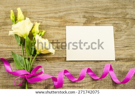 Empty postcard, colorful flowers and ribbon on wooden background