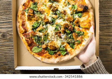 Woman\'s hand taking one piece of pizza from cardboard pizza box. Top view
