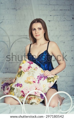 Young beautiful woman wearing sexy blue nightgown sitting on the bed, holding pillow