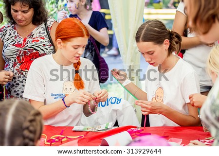 ZAPOROZHYE, UKRAINE - SEPTEMBER 5, 2015. Volunteers at bracelets braiding workshop during family festival organized by Charity Fund Child`s Smile for citizens and Donetsk refugees, financed by USAID