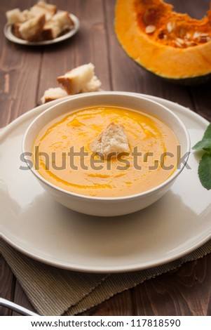 Bowl of pumpkin soup with bread crouton on white wood table