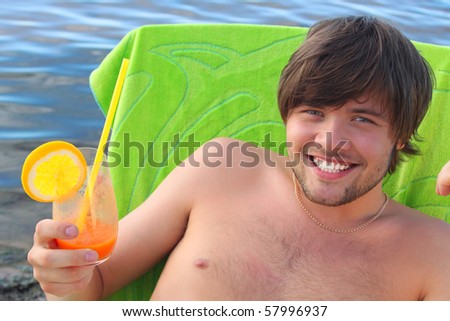Young beautiful man relaxing at the seaside with a glass of fresh juice