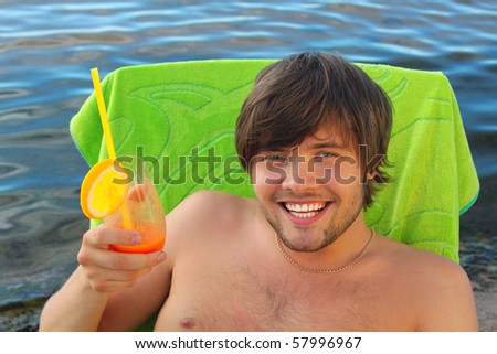 Young handsome man drinks fresh orange juice at the seaside