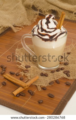 Iced coffee with foam and cinnamon on canvas and wooden background