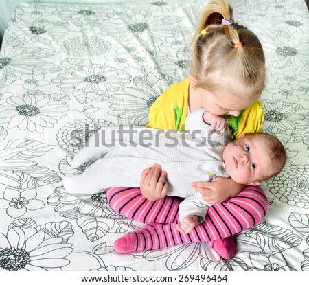 A girl holding in her arms her younger three month old sister sitting cross-legged on a bed.