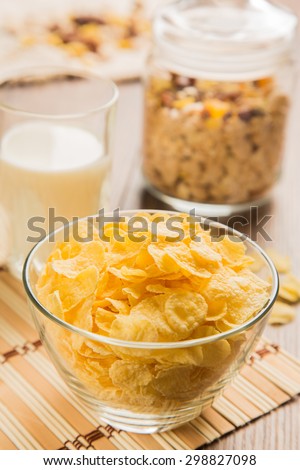 corn flakes in glass bowl with glass of milk and muesli on background